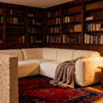 A warm, intimate living room nook featuring built-in dark wood bookshelves and a cream sofa, designed to create a protected sense of refuge and psychological enclosure.
