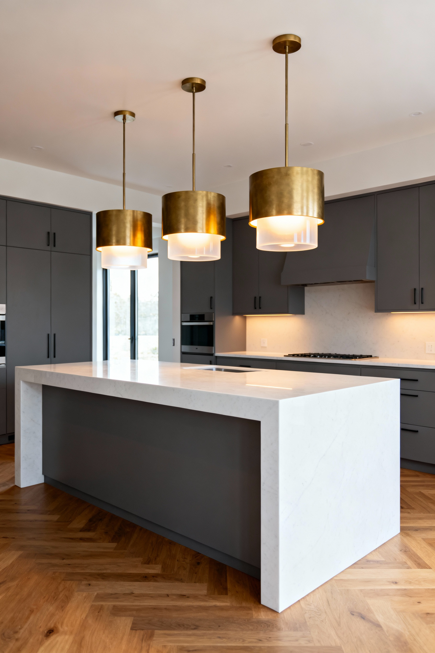 Three perfectly scaled brass drum pendant lights hanging above a long white quartz kitchen island, demonstrating ideal visual weight.