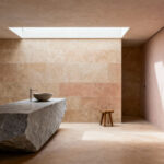 A serene, organic bathroom featuring walls and floors clad in matte mushroom-colored micro-cement and honed limestone, centered around a substantial raw-cut slate vanity under soft, diffused natural lighting.