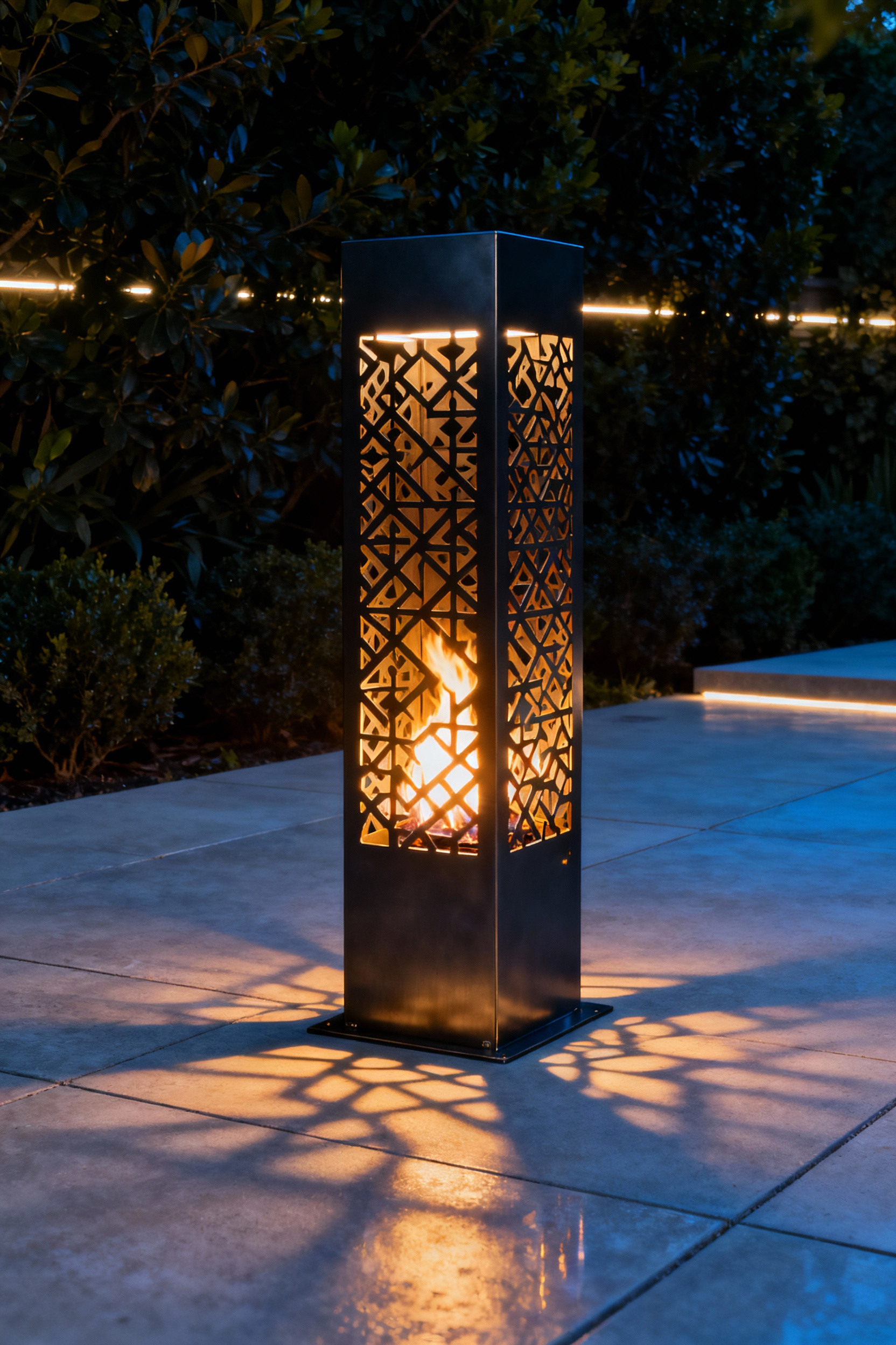 Modern outdoor firepit with a tall, anodized aluminum perforated metal enclosure, casting dramatic shadows on concrete paving at twilight from the flickering fire and subtle LED backlighting.