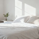 A serene, minimalist bedroom with clean lines and decluttered surfaces, illuminated by soft natural light. Represents the calm achieved through bedroom decluttering.