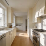 A bright and airy modern kitchen with warm white cabinetry, marble surfaces, and natural wood flooring, demonstrating the soft depth of gallery white paint.