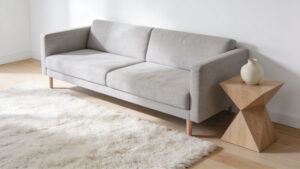 A wide-angle view of a minimalist living room showcasing ample negative space with white walls, a light gray linen sofa, and natural wood flooring, emphasizing organization and visual calmness to reduce cognitive load.
