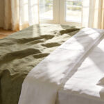 High-quality interior photo of a cozy bedroom featuring the textural contrast between soft rumpled linen and crisp structured percale bedding.